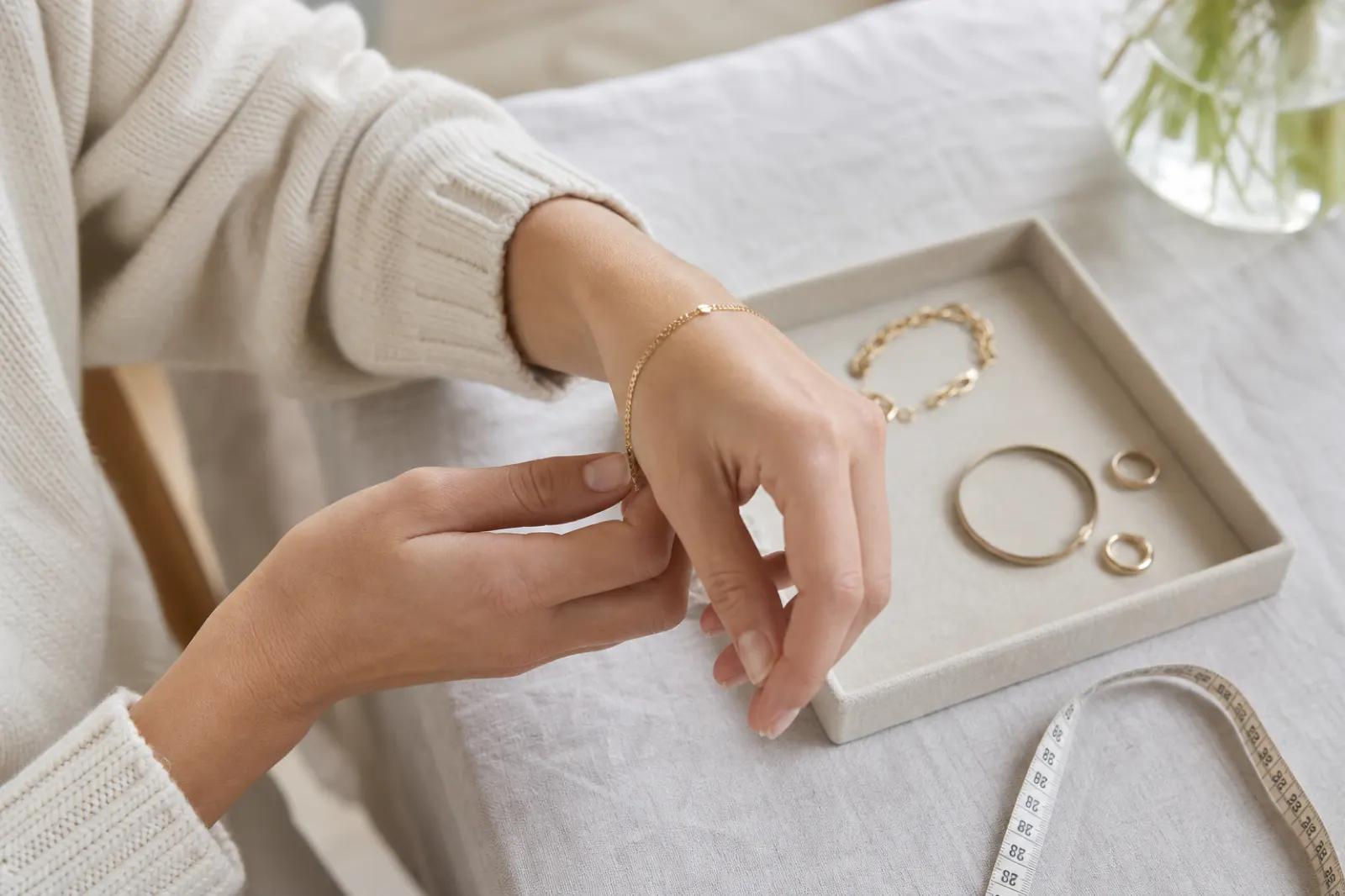 Person som provar ett tunt kedjearmband med armring och måttband vid en liten smyckesbricka
