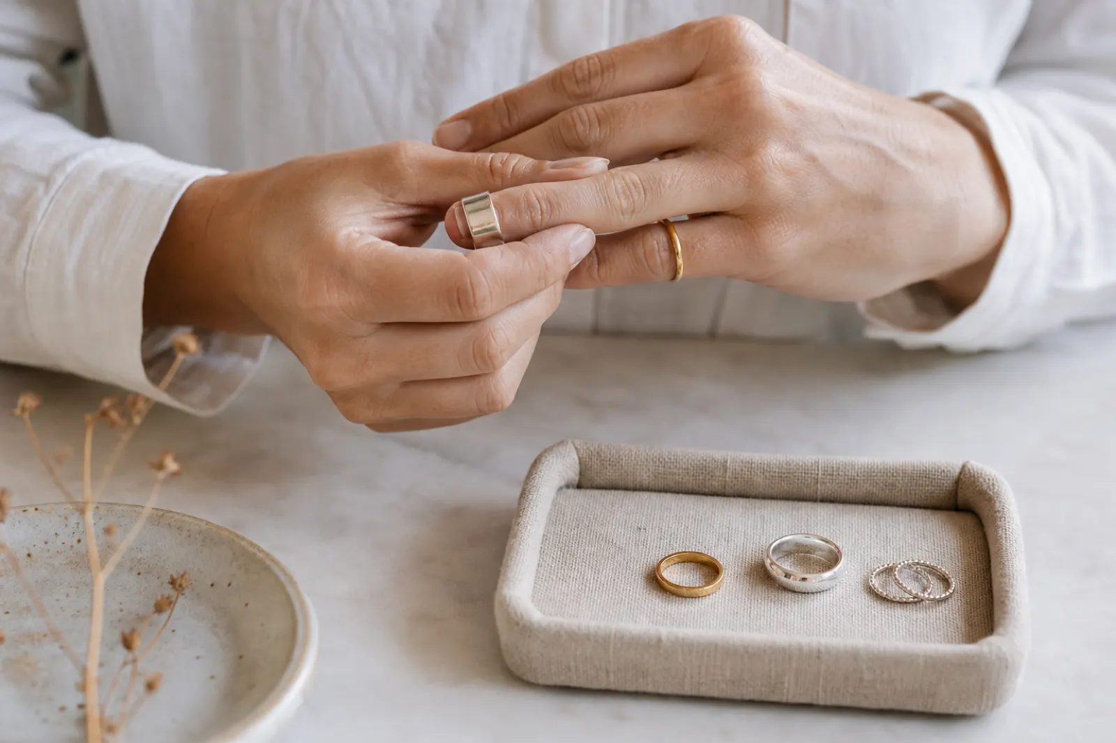 Händer som provar en bred silverring med guld- och silverringar på en liten smyckesbricka